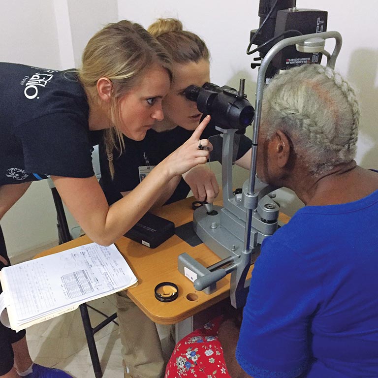 Two optometry students examine an elderly patient's eyes.