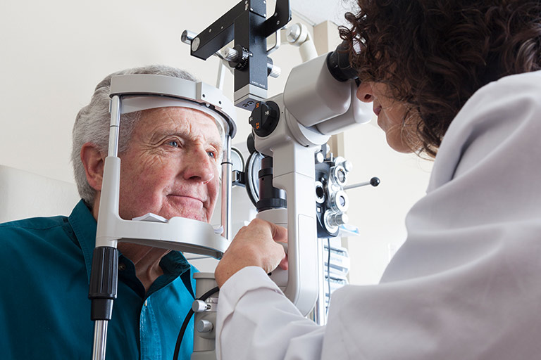 An optometry student uses a slit lamp to examine an elderly man's eyes