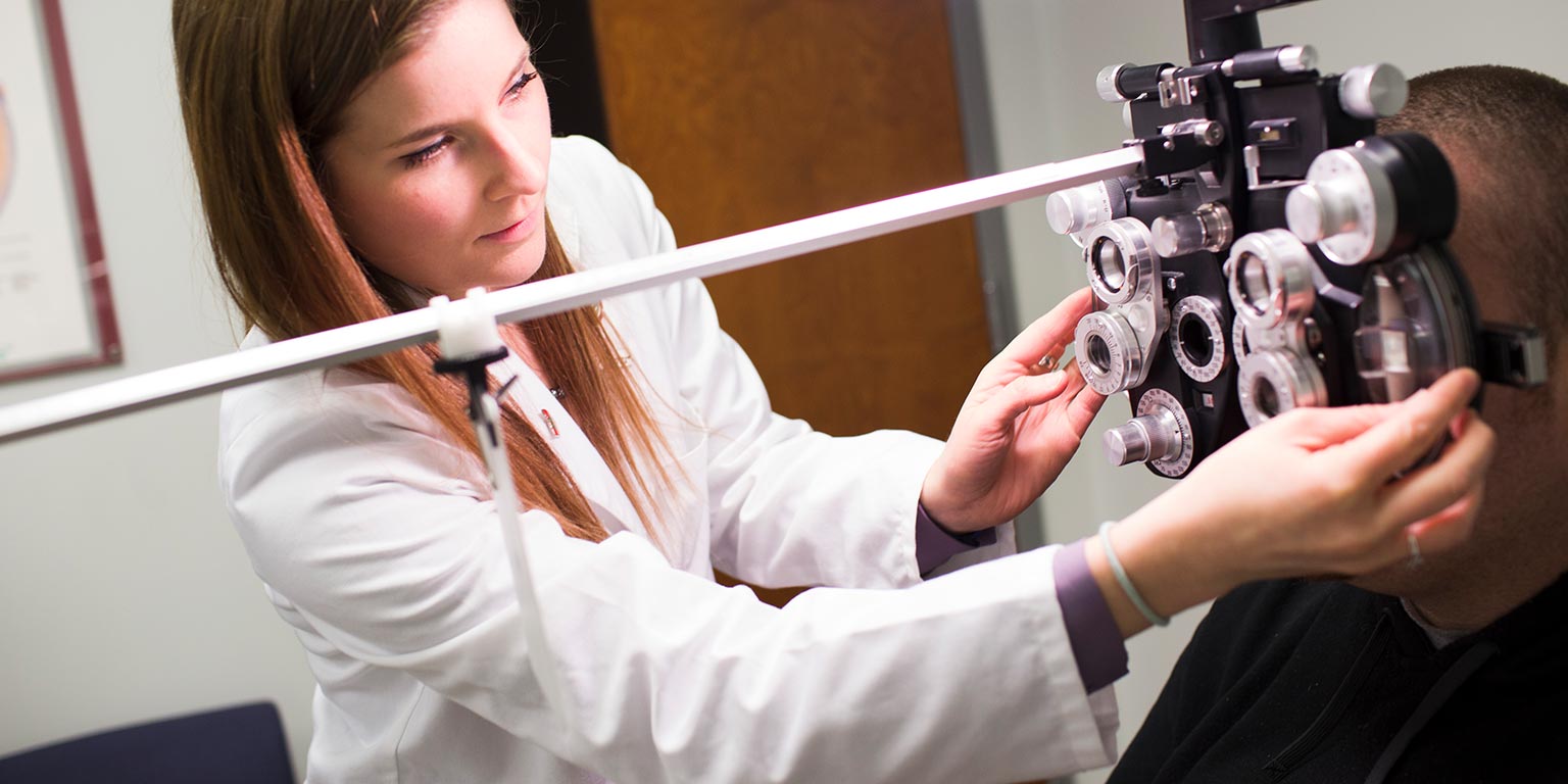 A student performs an eye exam using a phoropter.